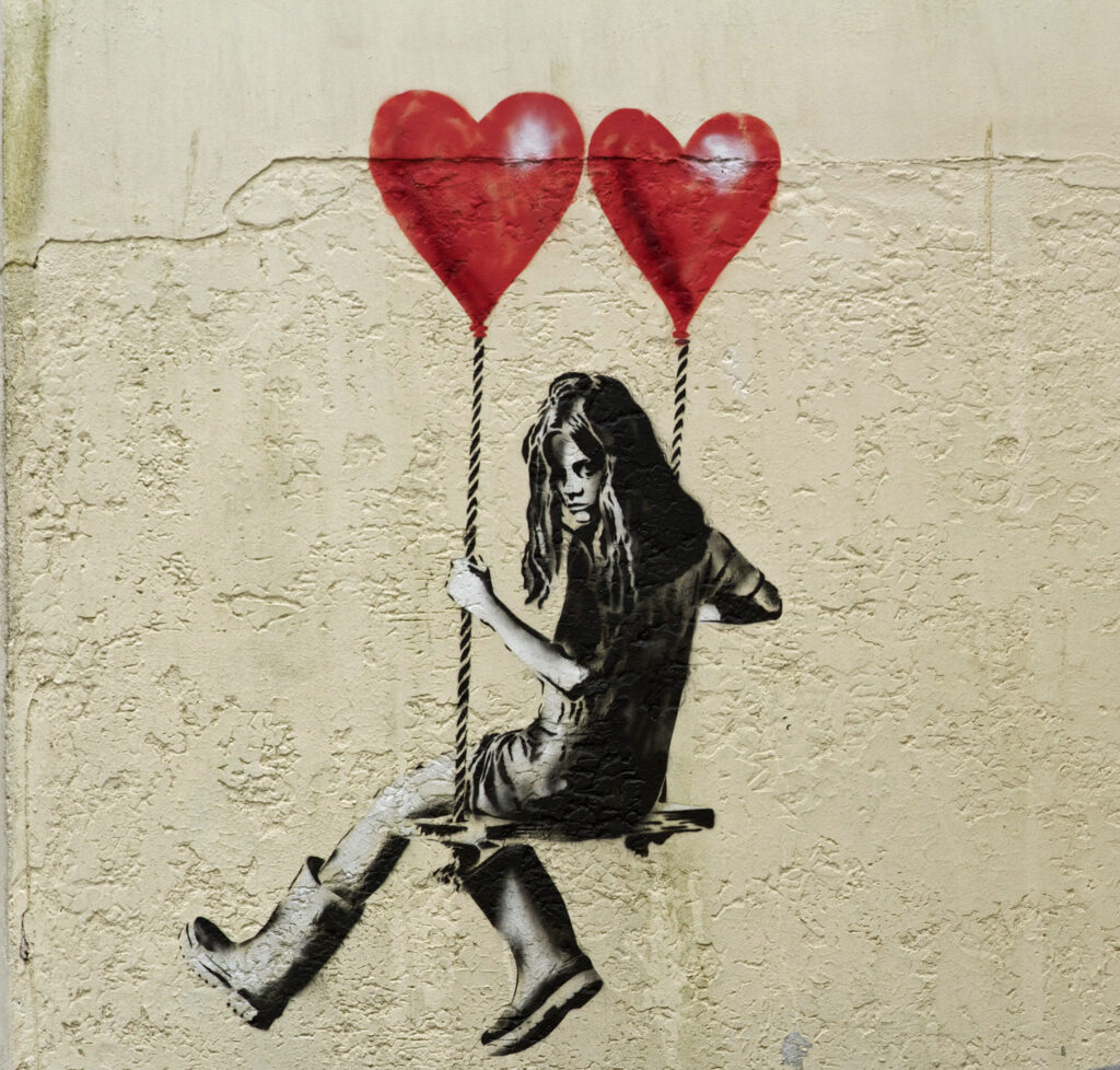 Girl sitting on a swing held up by two balloons street art